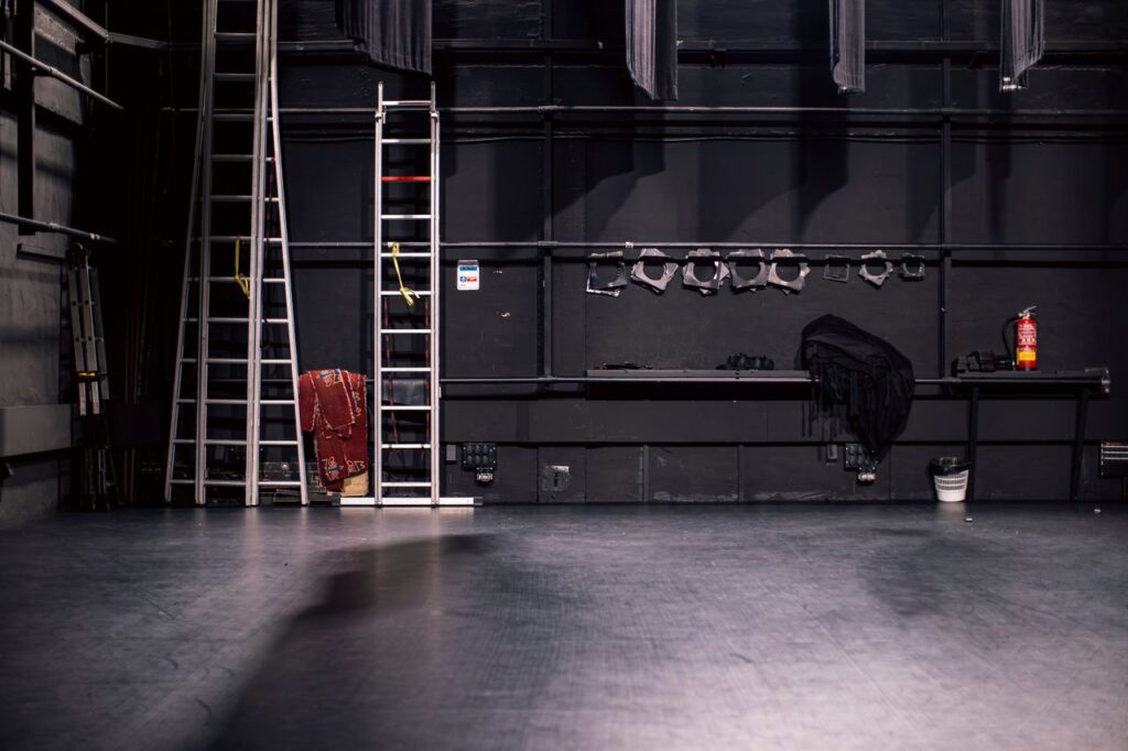 A quiet theater stage with ladders and equipment, ready for setup.